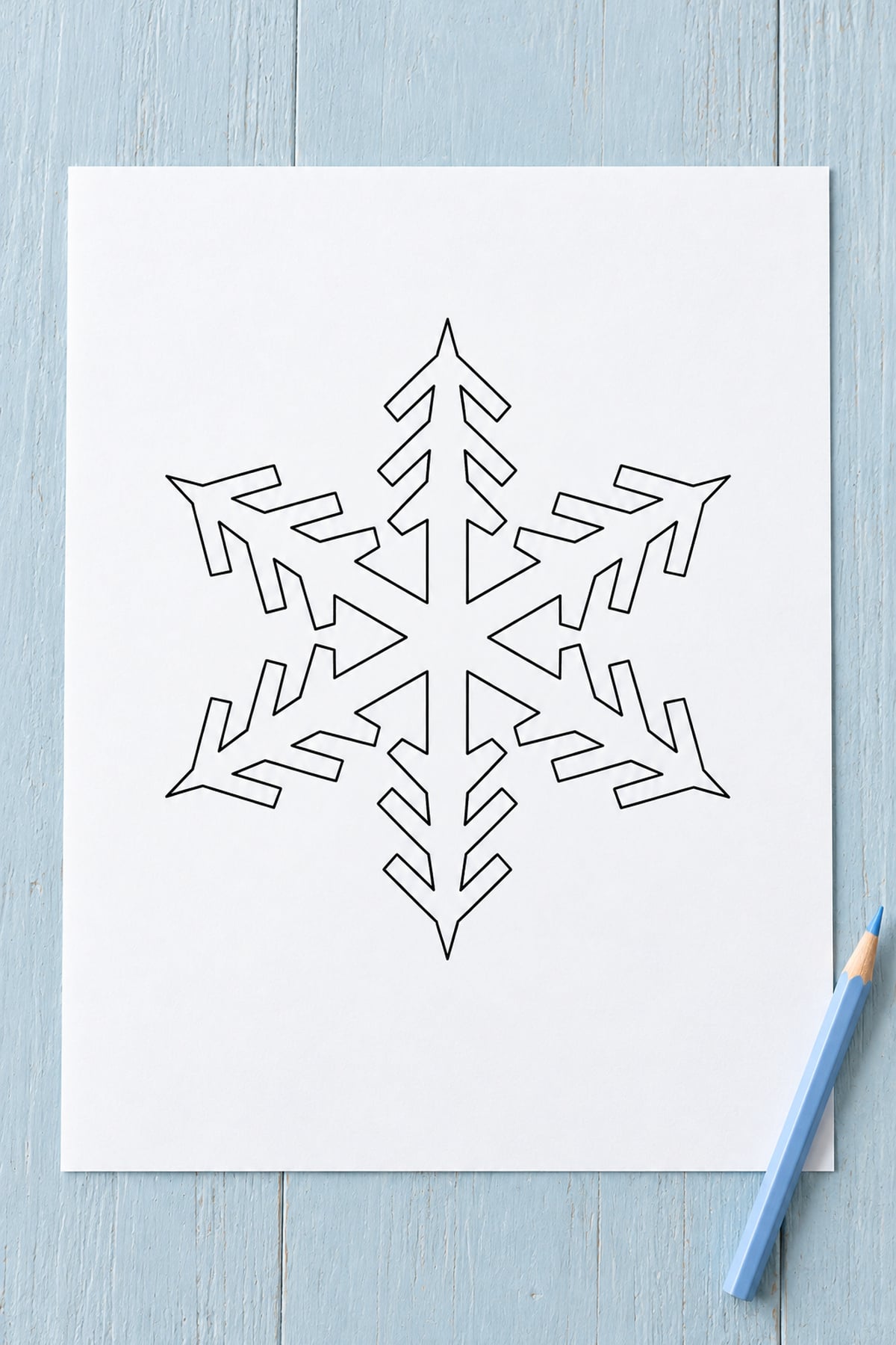 Feather-branch snowflake outline on white paper against pale blue painted wood beside a blue pencil.