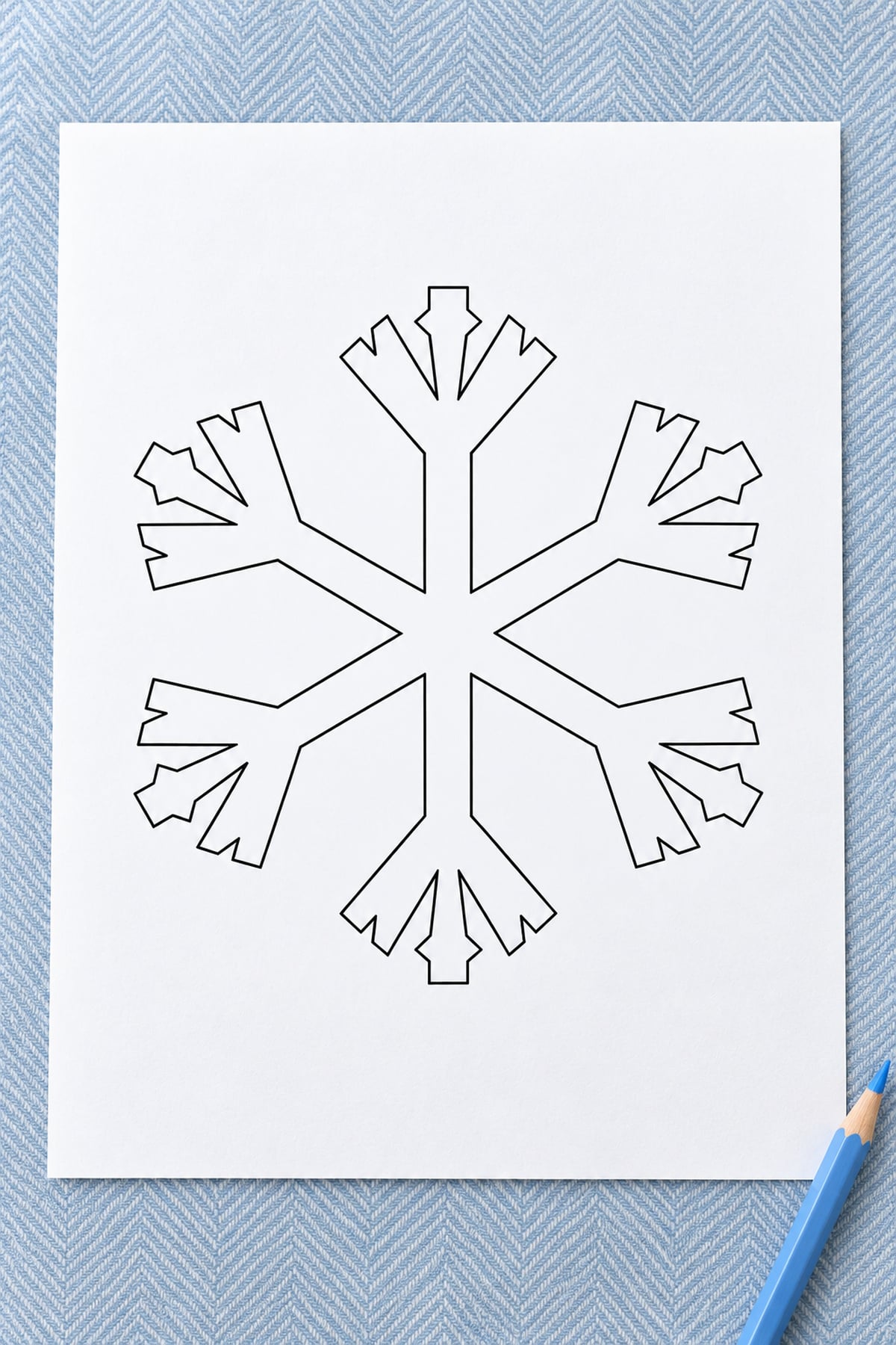 Triple-fork snowflake outline on white paper over blue herringbone fabric, with a blue pencil beside it.