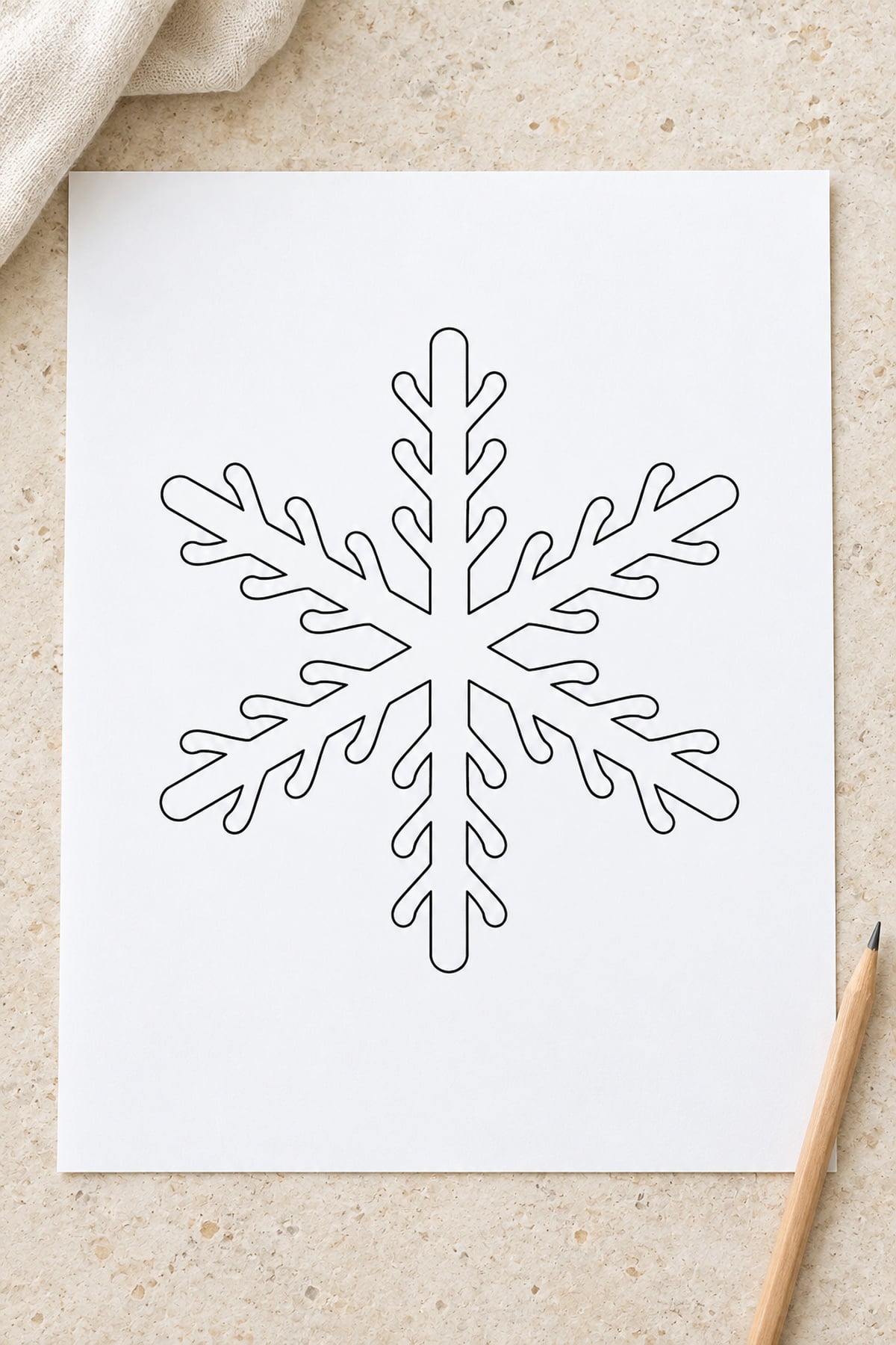 Antler-branch snowflake template on a cream stone surface with ivory linen and a wooden pencil.
