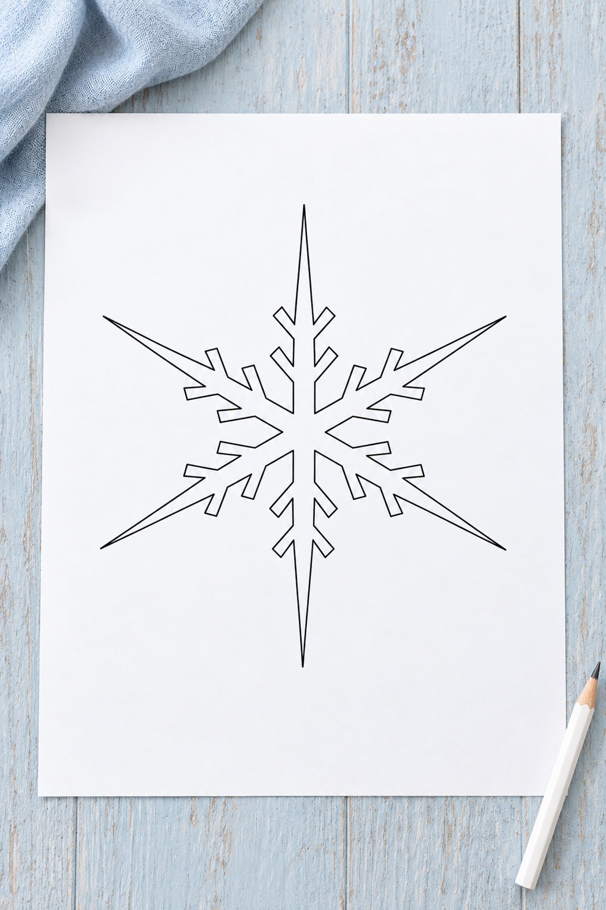 Long-icicle snowflake template on pale blue painted wood with blue fabric and a white pencil.