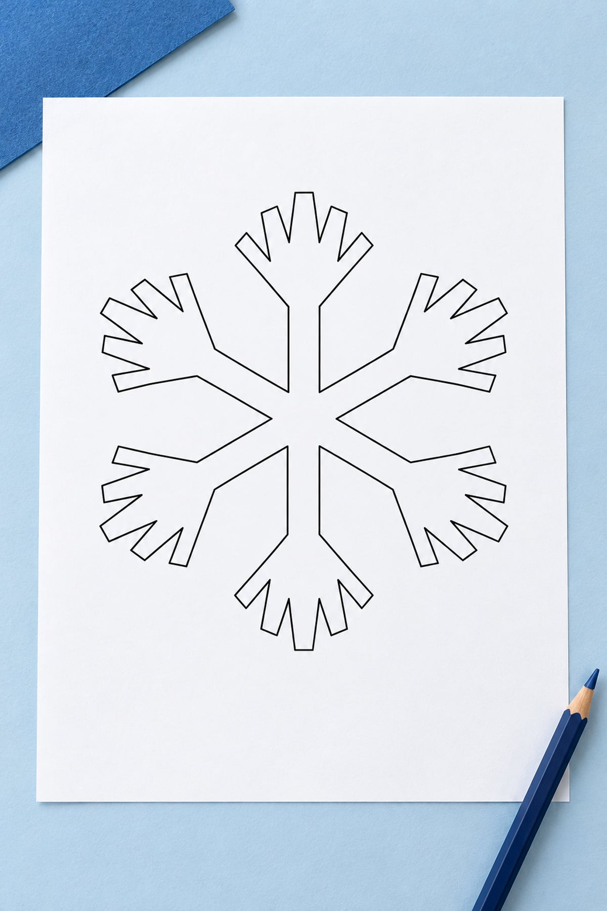 Starburst-branch snowflake template on a pale blue background with darker blue cardstock and a navy pencil.