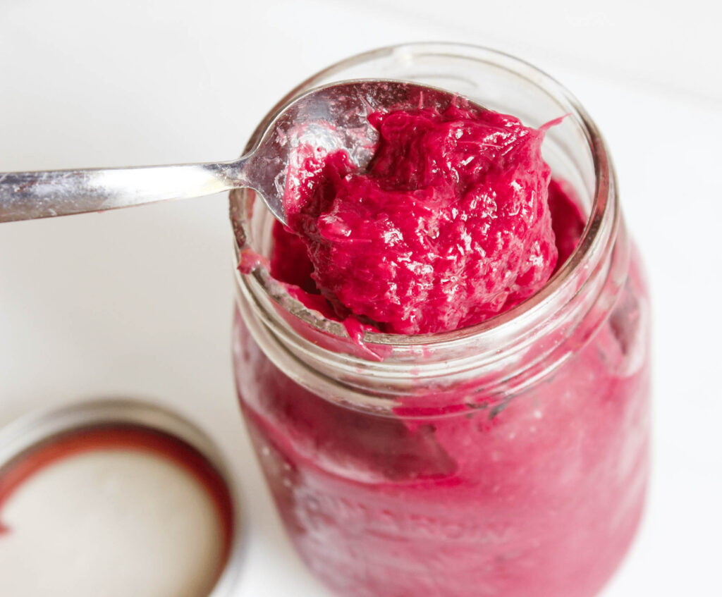 Healthy Strawberry Rhubarb Jam - open mason jar of red rhubarb and strawberry jam being scooped with spoon. Chia seeds added for thickness. || Nikki's Plate