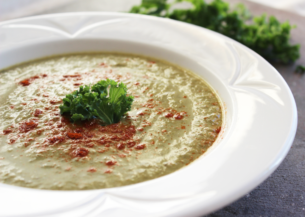 Round white bowl of spicy kale soup recipe with fresh kale and cayenne pepper. Green leafy kale chopped.Base of potato and vegetable broth. Vegan, dairy free and gluten free. || Nikki's Plate