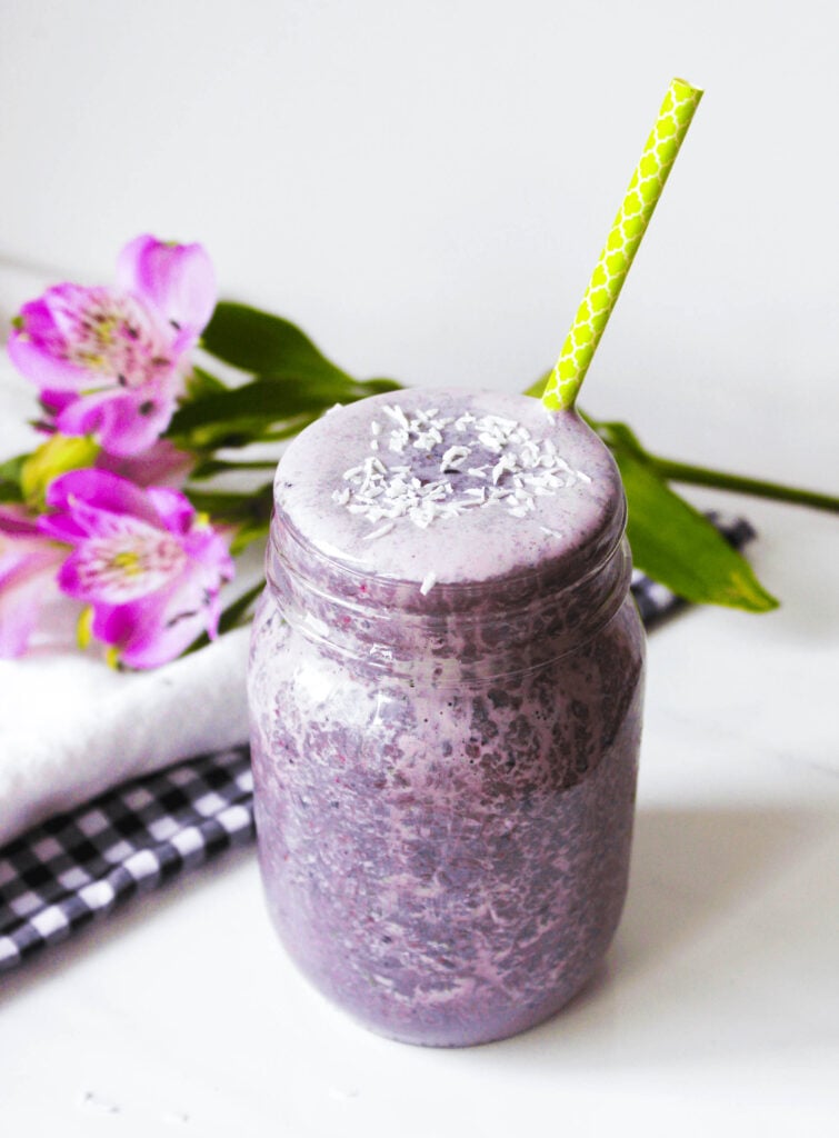 side photo of berry lemon smoothie in mason jar, purple fruit smoothie, green straw, cold beverage, breakfast drink.