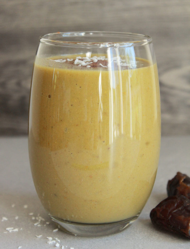 Vegan Pumpkin Pie Protein Smoothie; tall glass yellow drink, medjool dates surrounding