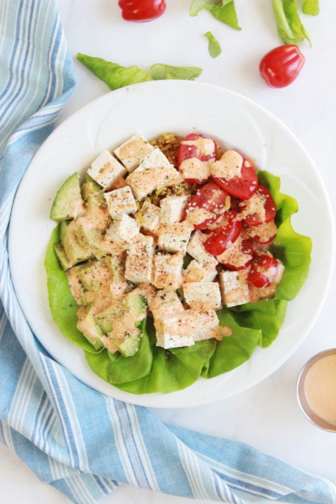 A delicious vegan buddha bowl packed with tofu, cherry tomatoes, and a sriracha tahini sauce