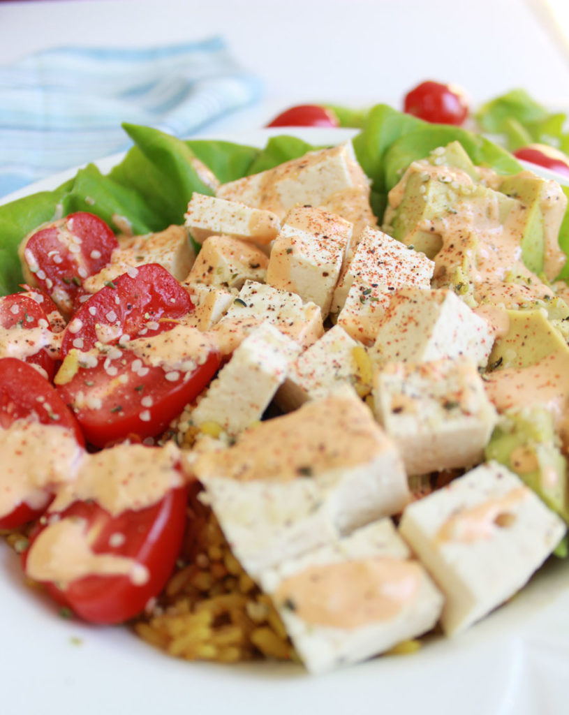 This buddha bowl has seasoned tofu, brown rice and juicy cherry tomatoes all topped with a creamy sriracha tahini dressing