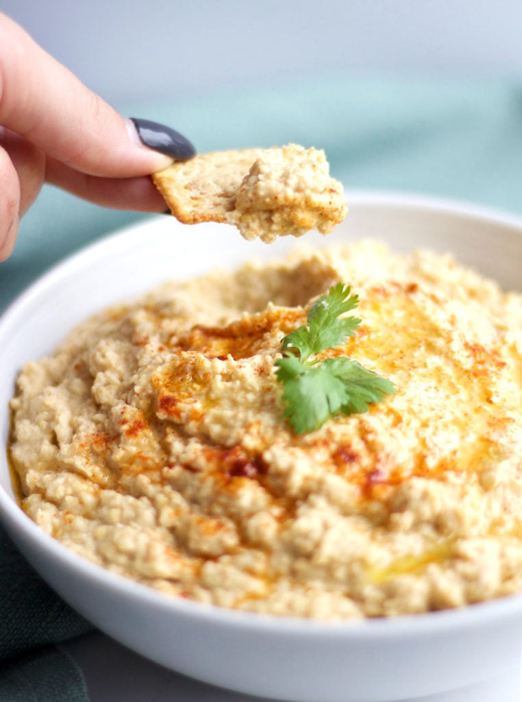 Bowl of Spicy Chipotle Hummus with a cracker dipping into it for a snack || www.nikkisplate.com