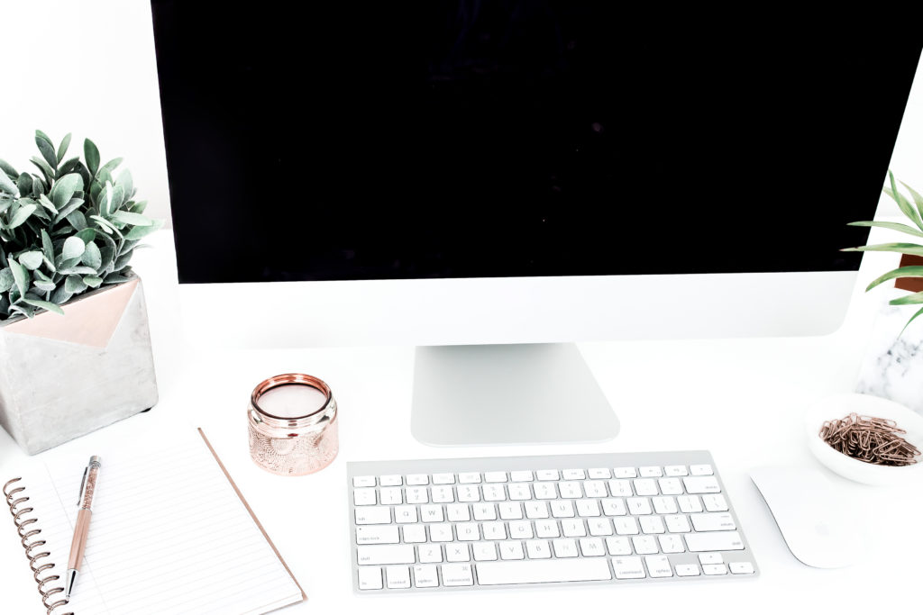 A blogger's workspace; a computer surrounded by plants, a candle, and a notebook and pen