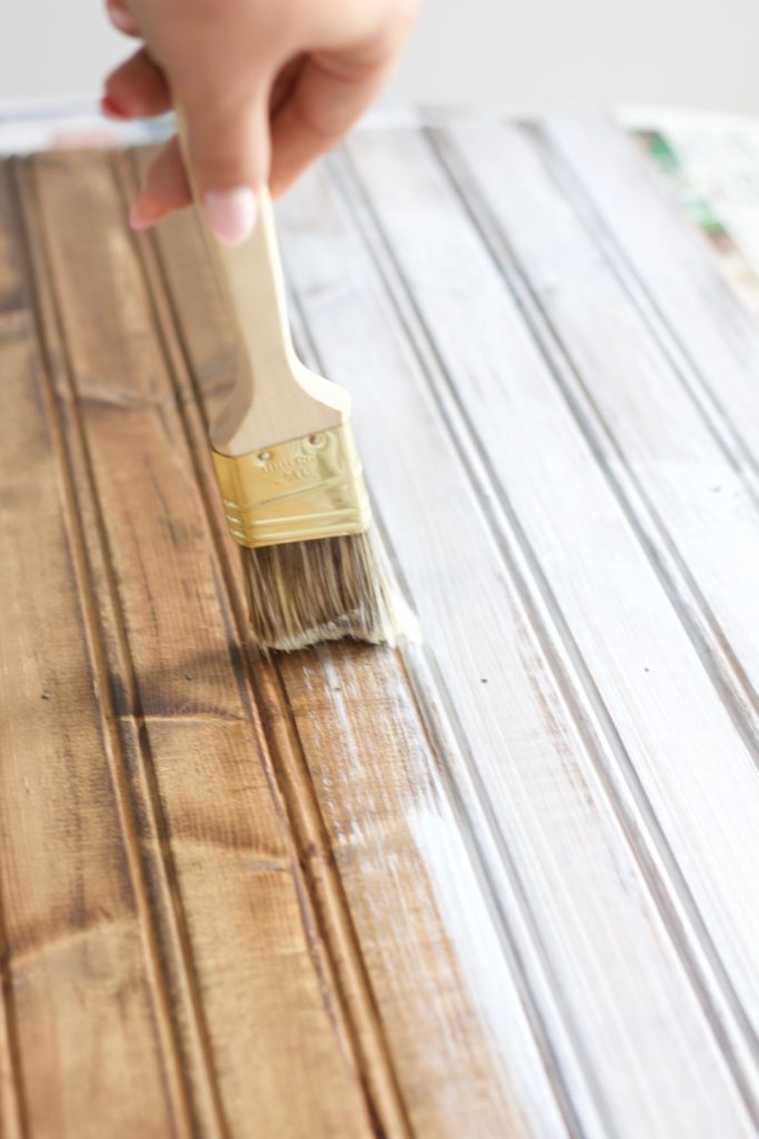 Use a very thin light layer of white paint over the wood stain to begin whitewashing