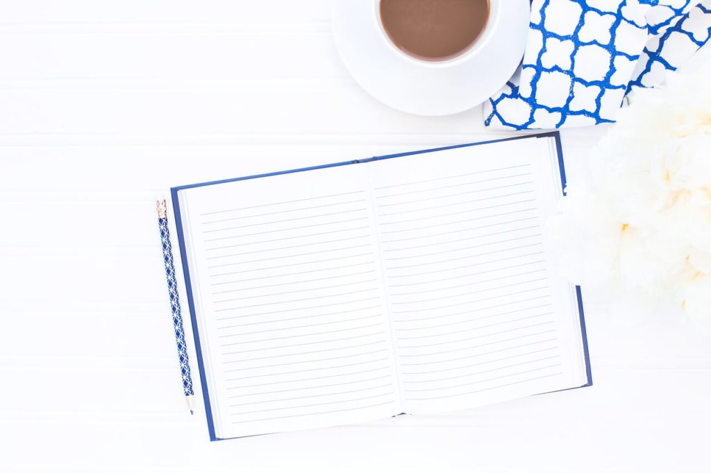 A notebook and pencil on a table with flowers and a cup of coffee