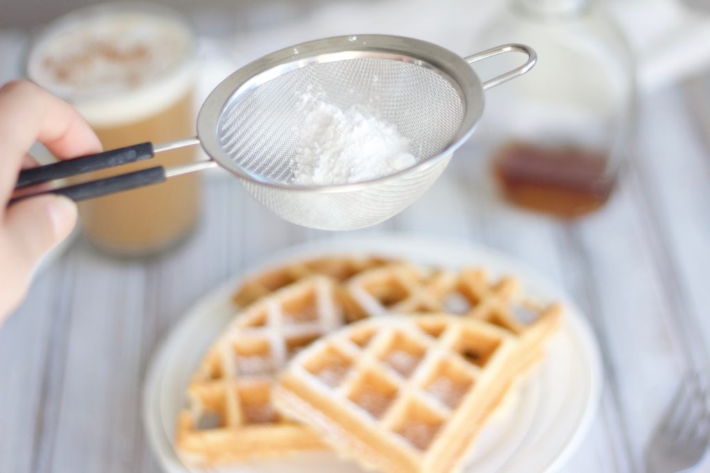 Dusting powdered sugar over fresh, homemade dairy free waffles