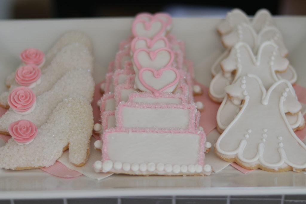 Decorated sugar cookies in the shape of shoes, wedding cake, and wedding dresses