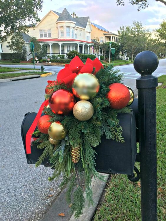 This Christmas mailbox has a large red bow, some bright and shiny Christmas ornaments, and fresh pine tree branches