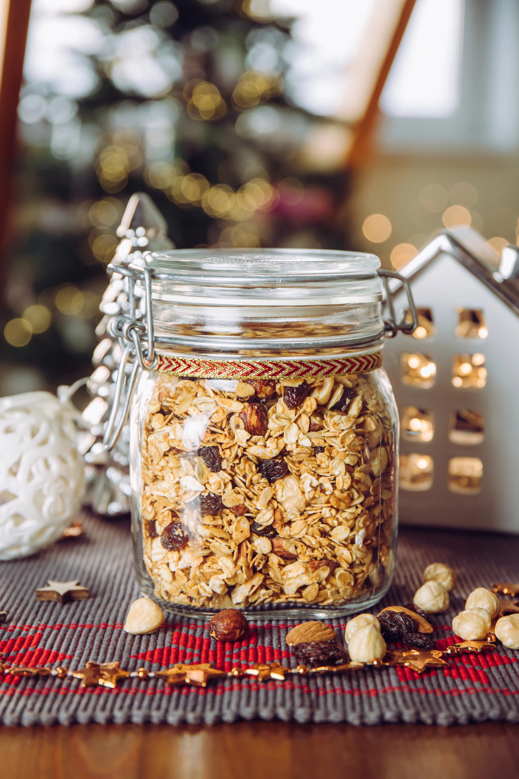 Homemade roasted granola with nuts and raisins in a Mason jar decorated with festive ribbon, a healthy DIY gift idea.