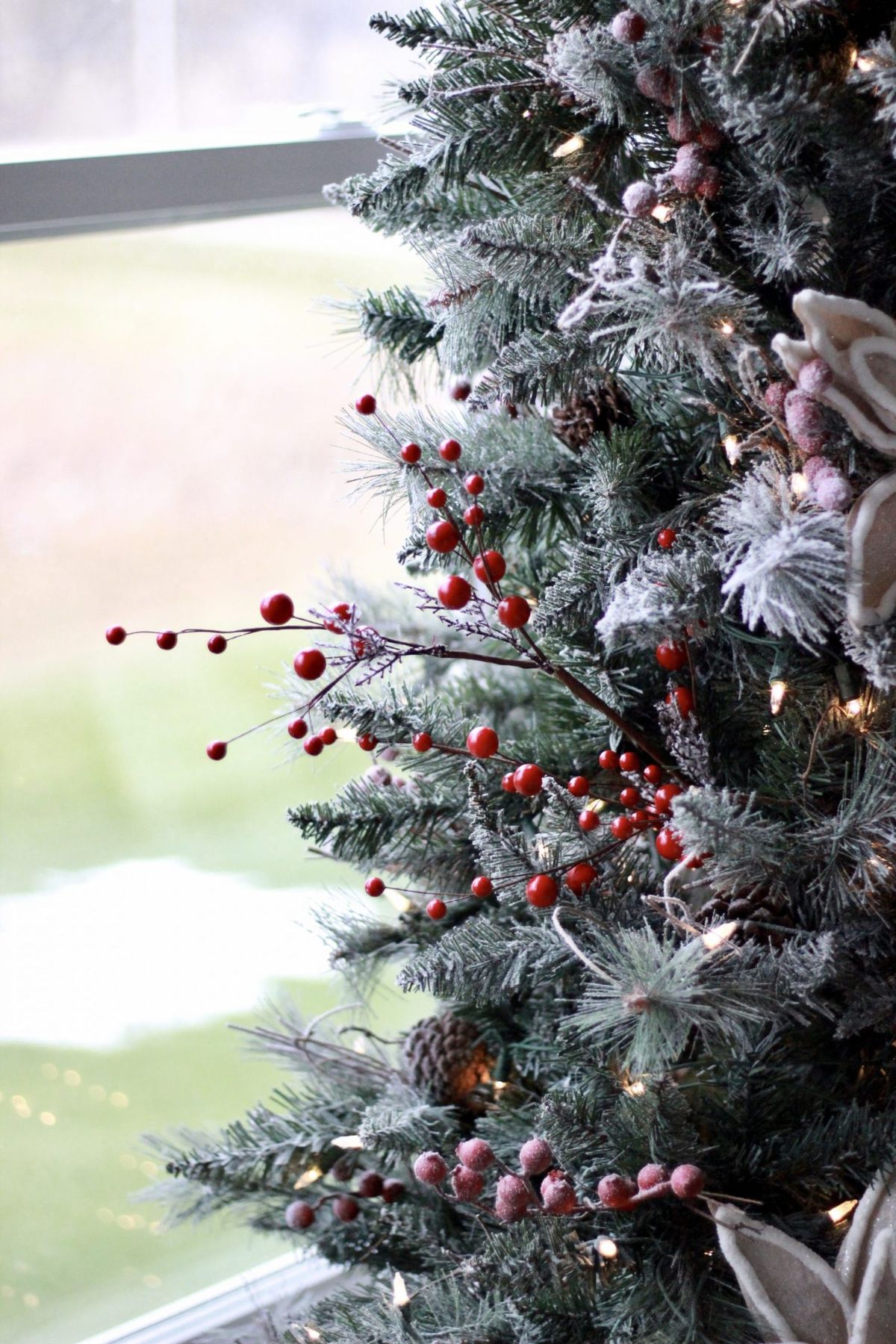 Close-up of a frosted Christmas tree decorated with red berries, pinecones, and greenery for a natural, textured holiday look.