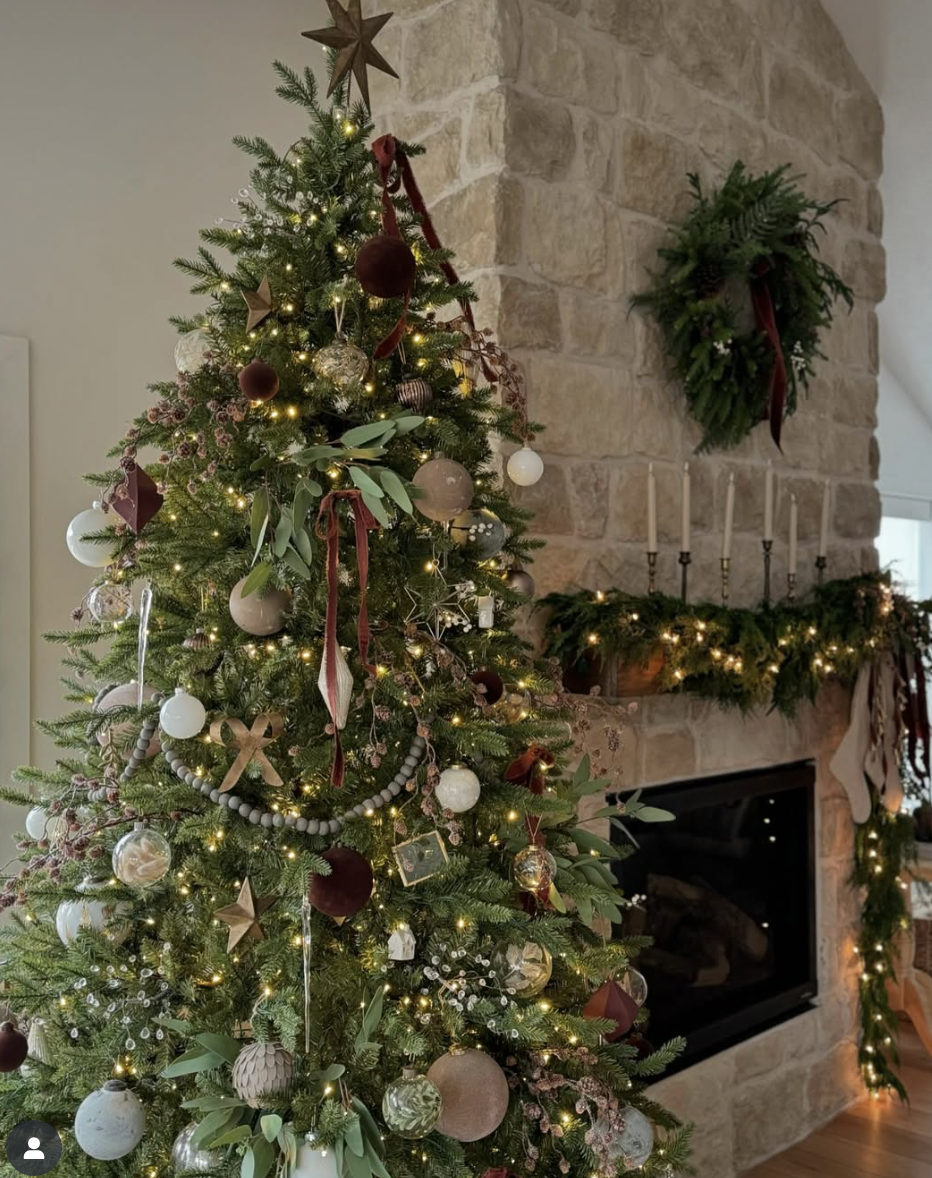 Cozy farmhouse living room with a Christmas tree decorated in earthy tones, velvet ribbon, and twinkle lights beside a stone fireplace.