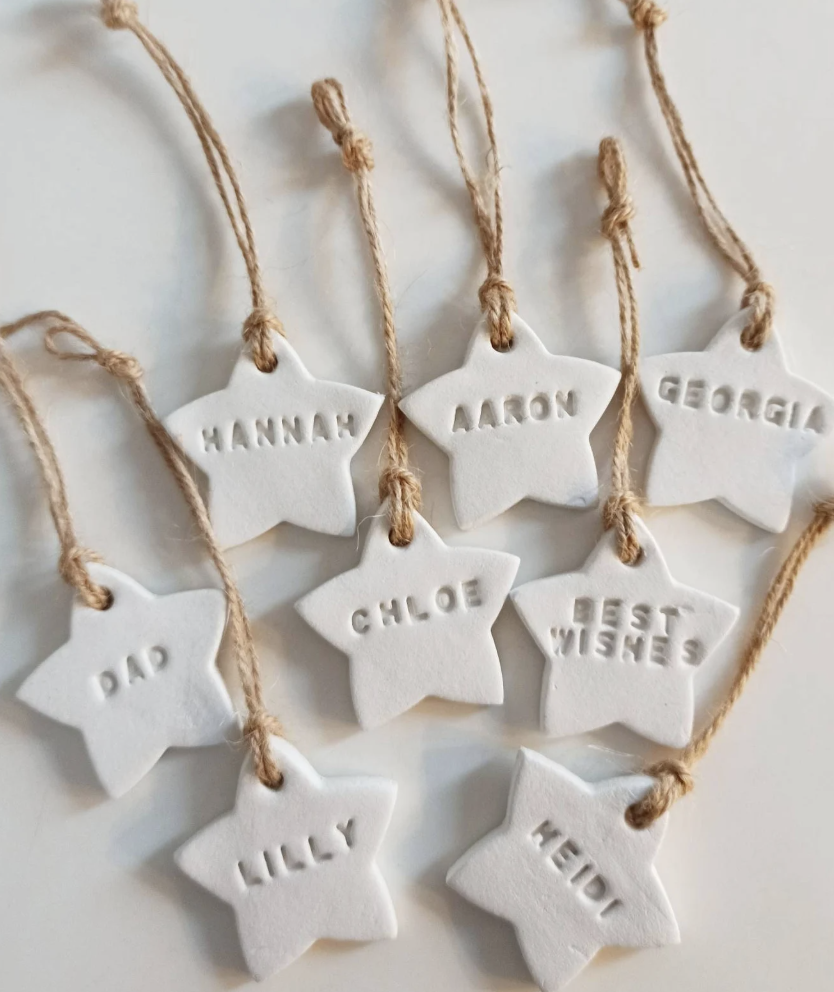 Handmade white clay star ornaments with names stamped into them and twine ties for a personalized DIY Christmas tree decoration.