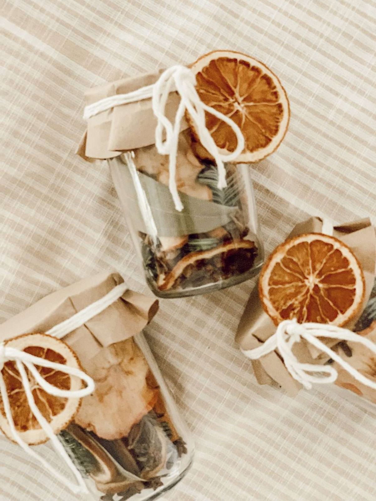 DIY holiday simmer pot Mason jar gift filled with dried oranges, spices, and wrapped in paper with string, a cozy homemade Christmas gift idea.