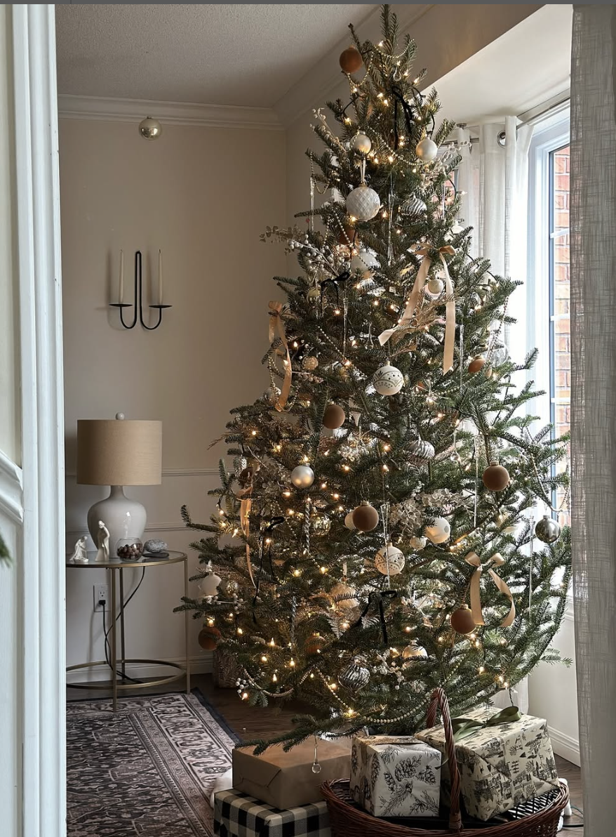 Elegant Christmas tree decorated with gold and black ribbons, white ornaments, and warm twinkle lights in a cozy neutral living room.