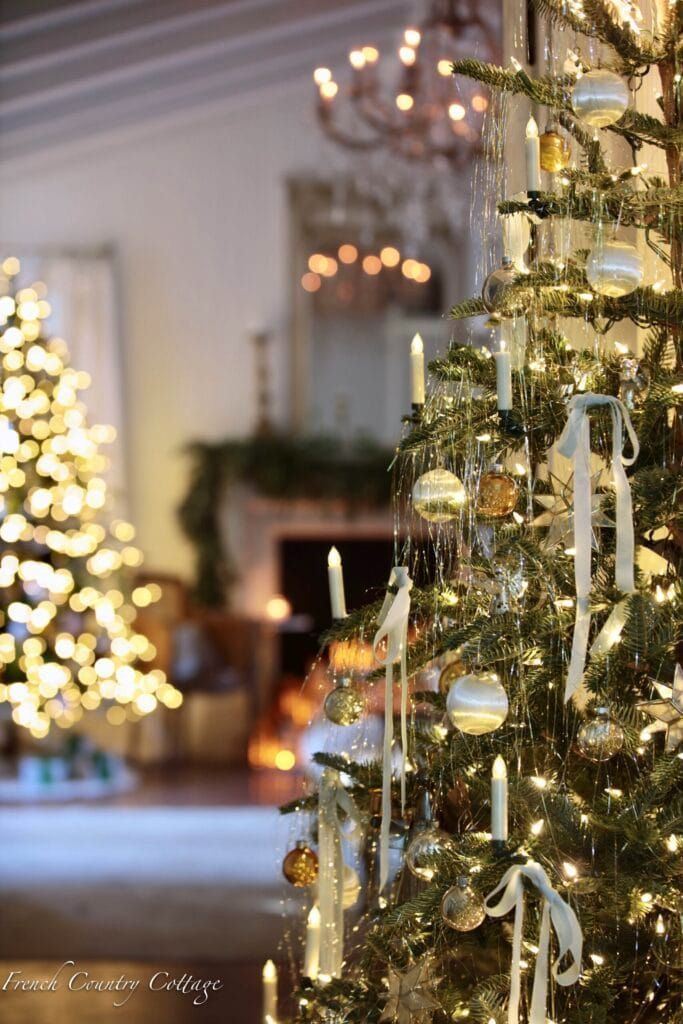 Elegant Christmas tree with gold and silver tinsel garland, white ribbon, and candle lights creating a glamorous vintage-inspired holiday look.