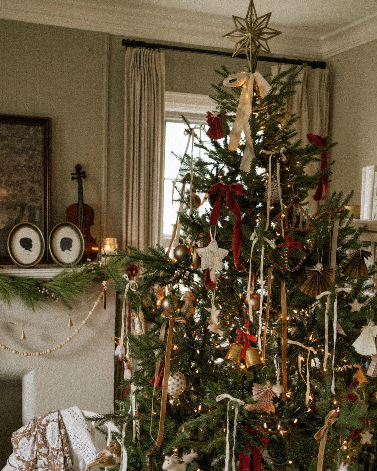 Cozy Christmas tree decorated with gold, burgundy, and neutral ornaments, ribbons, and a gold star topper showcasing 2025 holiday color trends.