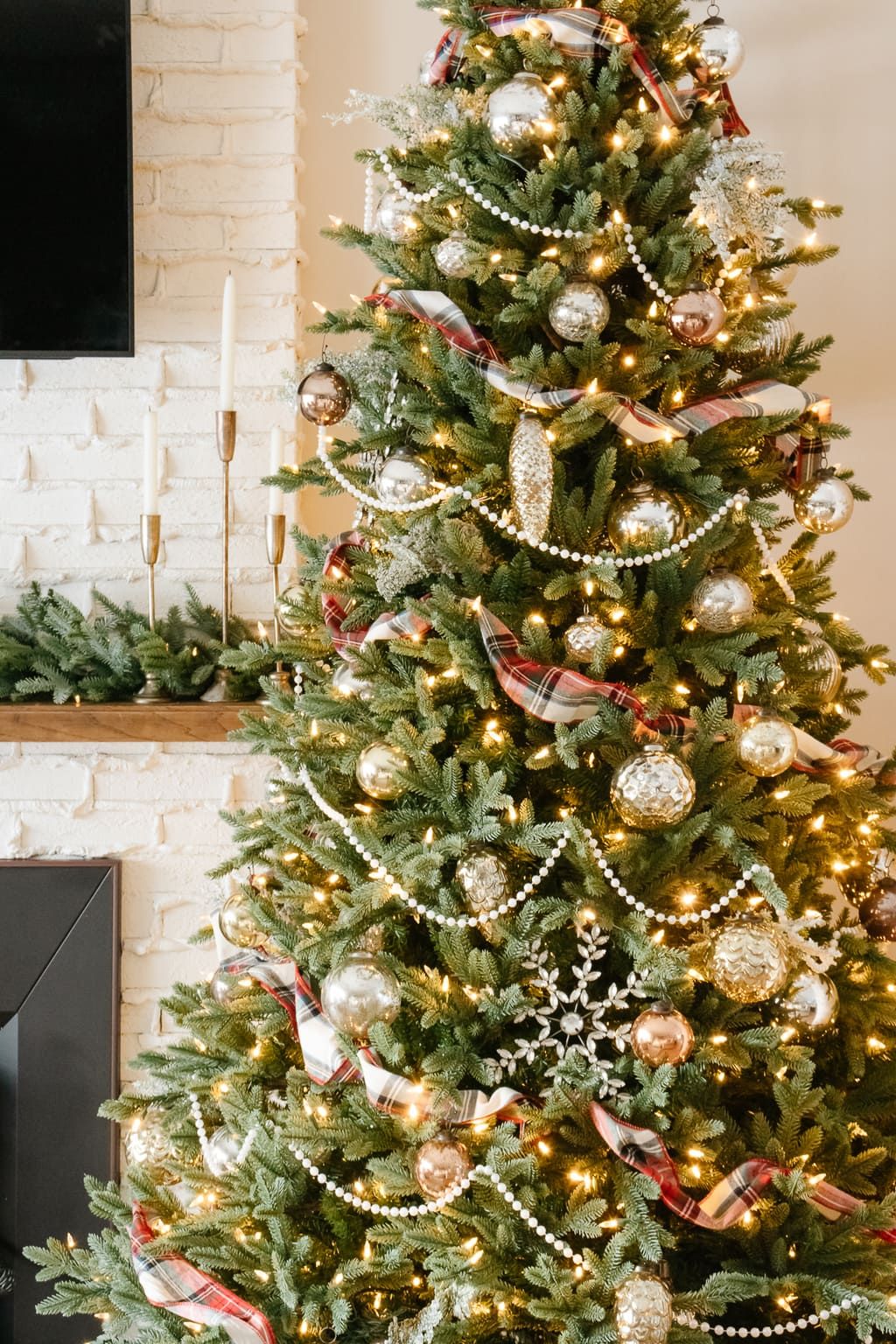 Christmas tree decorated with wooden bead garland, metallic ornaments, and plaid ribbon for a cozy farmhouse holiday style.