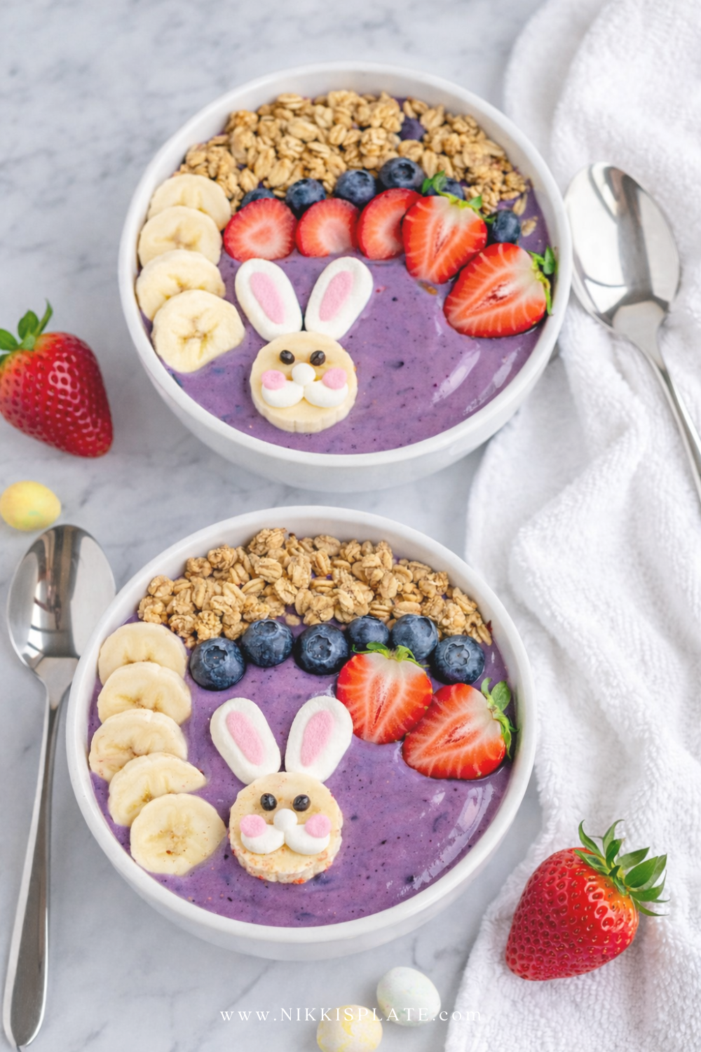 Purple Easter smoothie bowl topped with granola, strawberries, blueberries, banana slices, and a bunny face design
