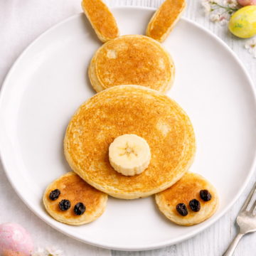 Sourdough Easter bunny pancakes shaped like a bunny on a white plate with banana slice tail and raisin details
