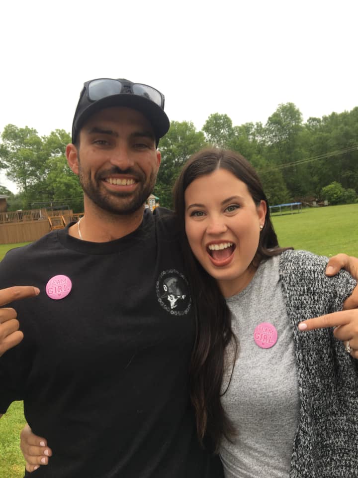 Gender Reveal Party - mom and dad pointing to "Team Girl" badges on shirts.