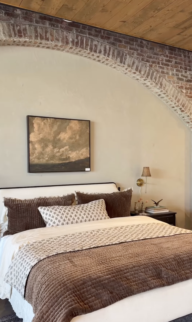 Joanna Gaines inspired farmhouse bedroom with rustic brick arch, wood ceiling, neutral bedding, and warm brown layered textiles.