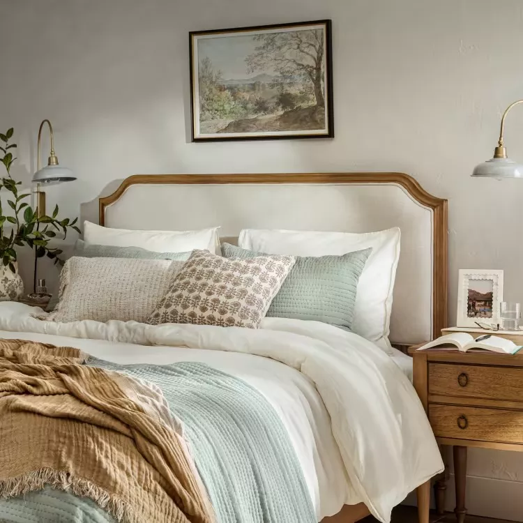 Joanna Gaines inspired neutral farmhouse bedroom with a wood headboard, layered bedding, vintage nightstand, and soft earth-toned textiles.