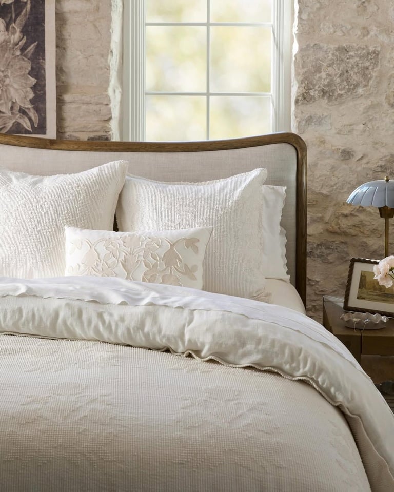 Joanna Gaines inspired farmhouse bedroom with rustic stone wall, neutral bedding, upholstered wood bed frame, and vintage bedside decor.