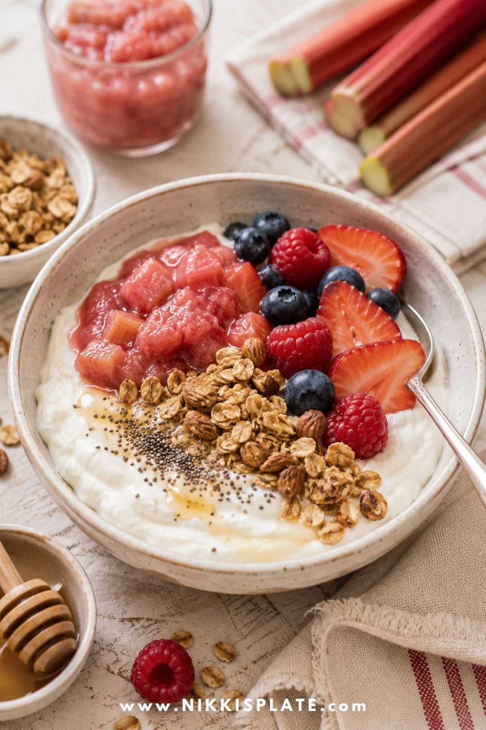 Healthy rhubarb yogurt bowl topped with rhubarb compote, fresh berries, granola, chia seeds, honey, and sliced strawberries.