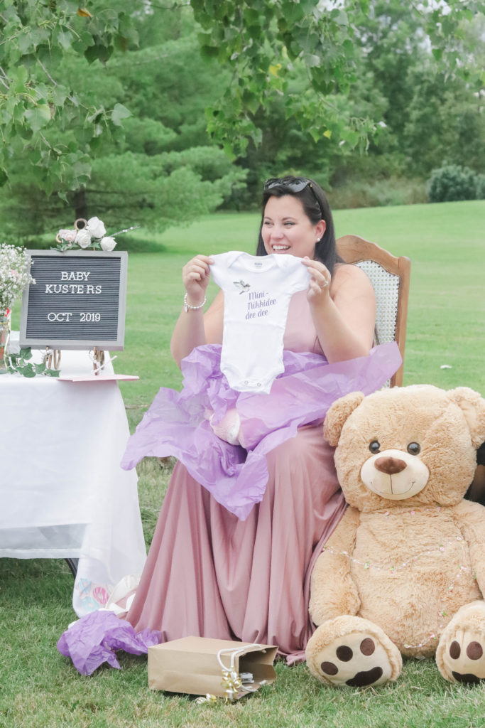 Nikki showing off a cute baby onesie at her pretty in pink baby shower.