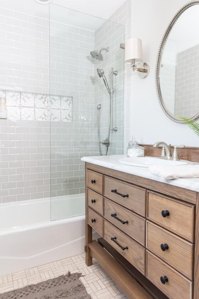 Best Bathrooms by Joanna Gaines; Fixer upper's top bathroom renovations by Joanna and chip Gaines! These rustic, country with hints of modern perfection bathrooms are everything #joannagaines #bathroom #bathrooms #renovations || Gray Tile, Grey subway tile, wood vanity, round mirror - Nikki's Plate