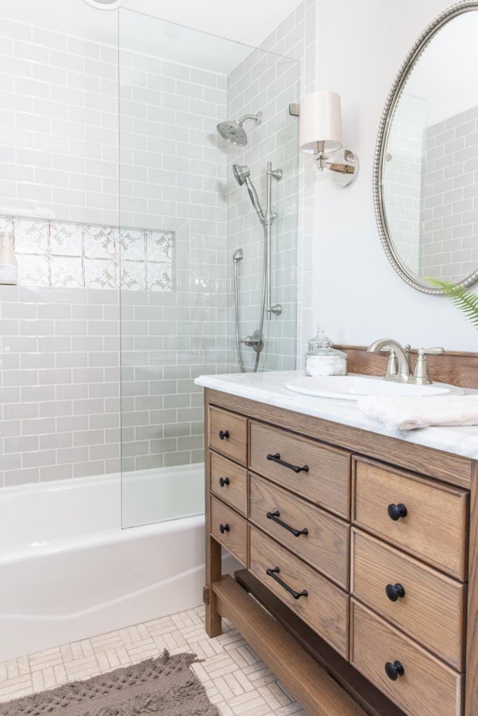 Best Bathrooms by Joanna Gaines; Fixer upper's top bathroom renovations by Joanna and chip Gaines! These rustic, country with hints of modern perfection bathrooms are everything #joannagaines #bathroom #bathrooms #renovations || Gray Tile, Grey subway tile, wood vanity, round mirror - Nikki's Plate