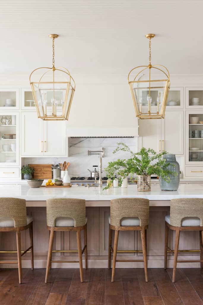 11 Best Kitchens by Studio McGee; These mordern industrial cage light fixtures go so well with the all-white color scheme of this kitchen. The breakfast bar chairs add color and texture!