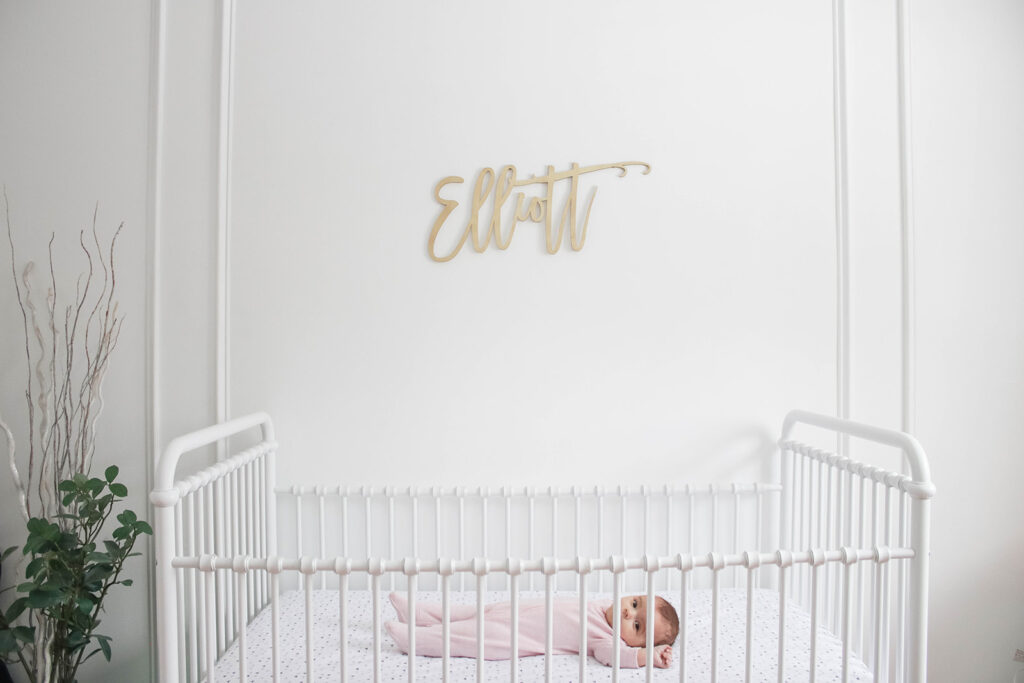 Elliott's White Vintage Crib; White walls, cursive name sign on wall, wainscotting, bright white baby girl room. #babygirlnursery || Nikki's Plate