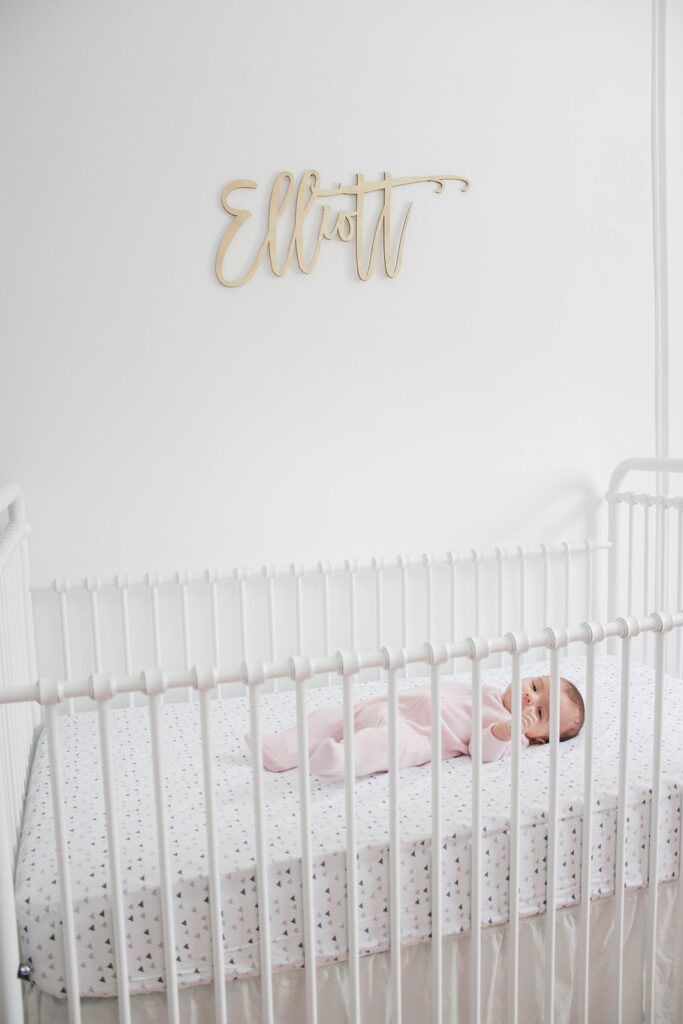 Elliott's White Vintage Crib; White walls, cursive name sign on wall, wainscotting, bright white baby girl room. #babygirlnursery || Nikki's Plate