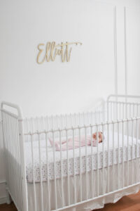 Elliott's White Vintage Crib; White walls, cursive name sign on wall, wainscotting, bright white baby girl room. #babygirlnursery || Nikki's Plate