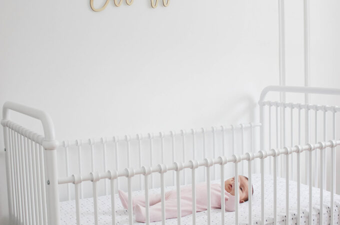 Elliott's White Vintage Crib; White walls, cursive name sign on wall, wainscotting, bright white baby girl room. #babygirlnursery || Nikki's Plate