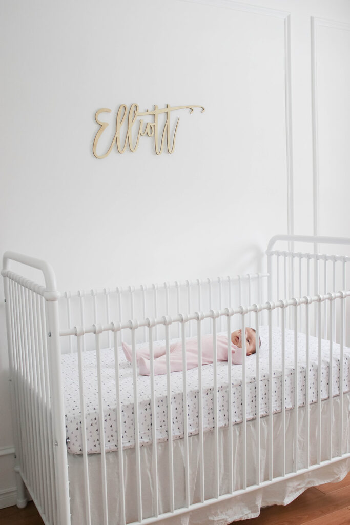 Elliott's White Vintage Crib; White walls, cursive name sign on wall, wainscotting, bright white baby girl room. #babygirlnursery || Nikki's Plate