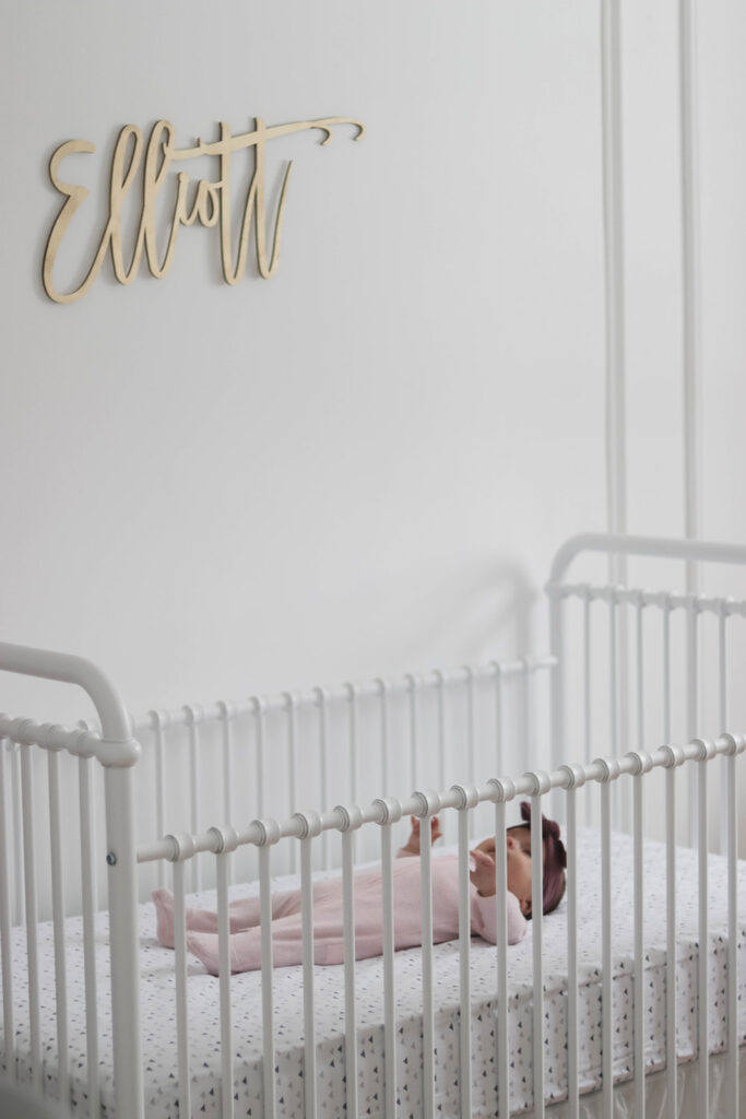 Elliott's White Vintage Crib; White walls, cursive name sign on wall, wainscotting, bright white baby girl room. #babygirlnursery || Nikki's Plate