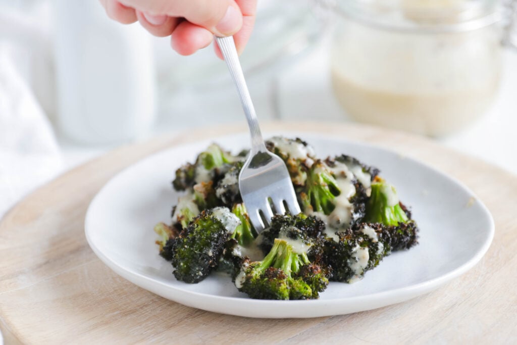 Fork eating Crispy Broccoli with Vegan Cheese Sauce; dairy and gluten free side dish for your vegan dinner! A nut free cheese sauce that you will love smothered on your blackened broccoli!