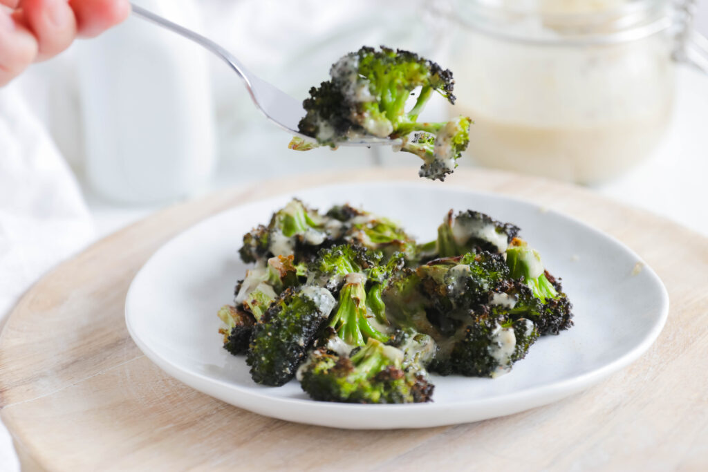 Fork lifting Crispy Broccoli with Vegan Cheese Sauce; dairy and gluten free side dish for your vegan dinner! A nut free cheese sauce that you will love smothered on your blackened broccoli!