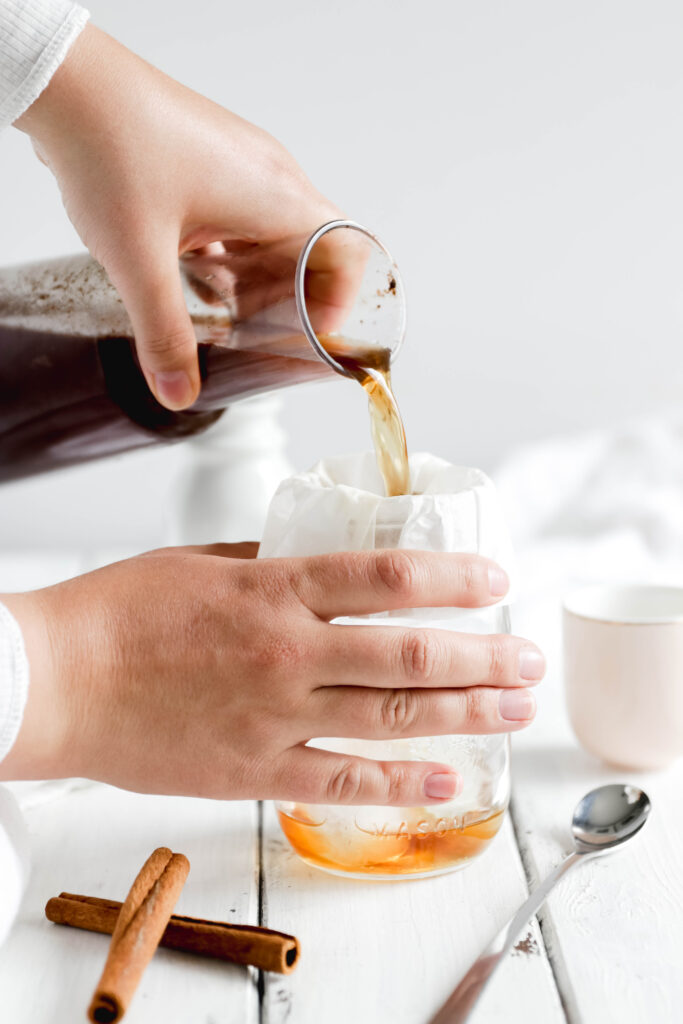 Pouring overnight cinnamon cold brew coffee over coffee filter on a mason jar