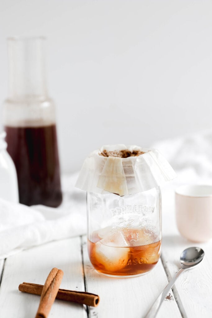 Overnight Cinnamon Cold Brew Coffee - coffee filter over mason jar to filter out coffee grinds. almond milk beside {vegan}