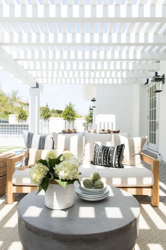 15 Deck Must Haves for Summer Entertaining; white and natural wood outdoor couch, stone coffee stable, white awning.