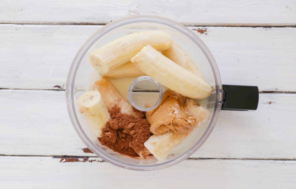 Food processor with ingredients for Chocolate Peanut Butter Ice Cream Cups; Vegan, dairy free and gluten free banana ice cream bites packed with cocoa and PB flavours.